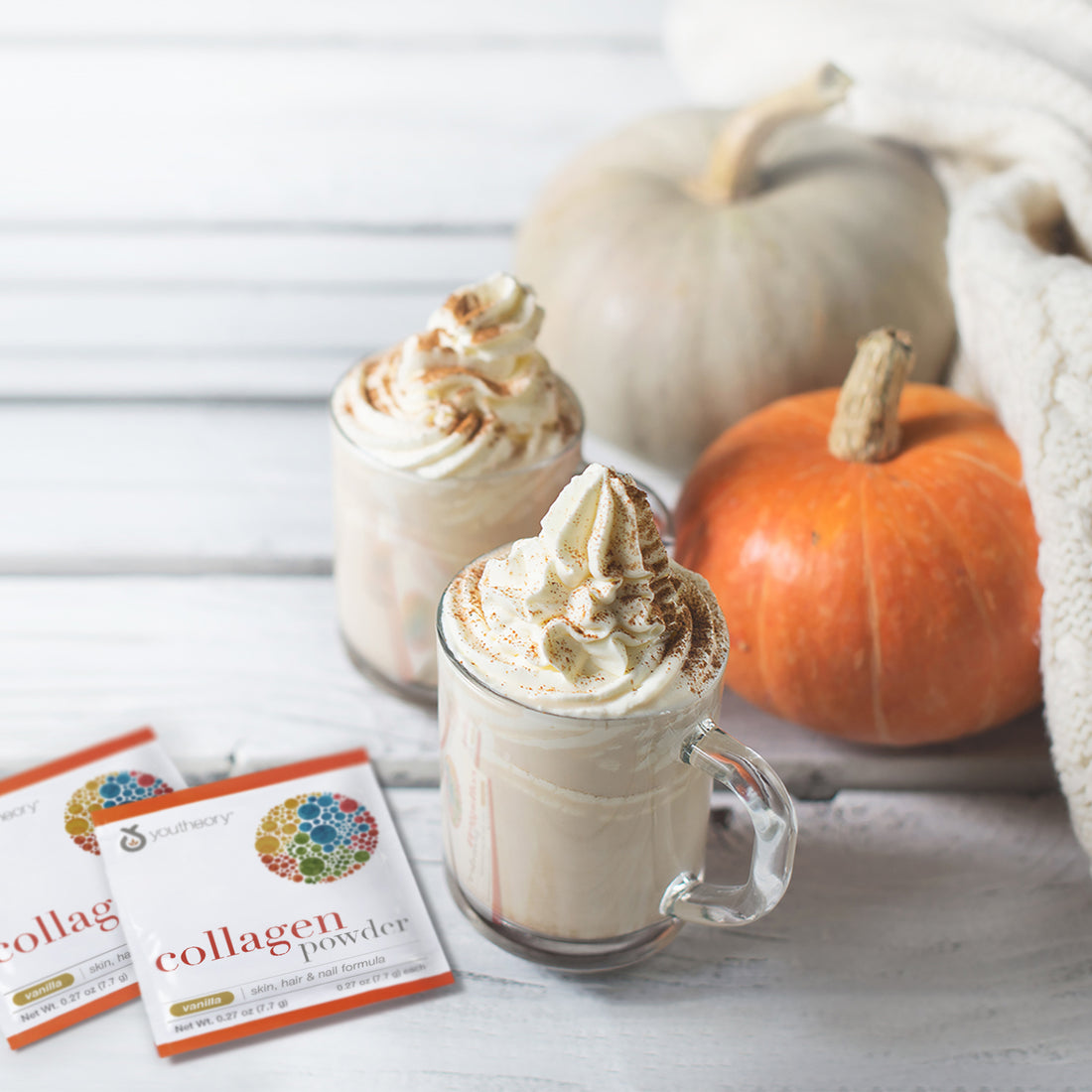 Collagen Powder packets next to Pumpkins spice latte with pumpkins and white cozy sweater over white wood texture.